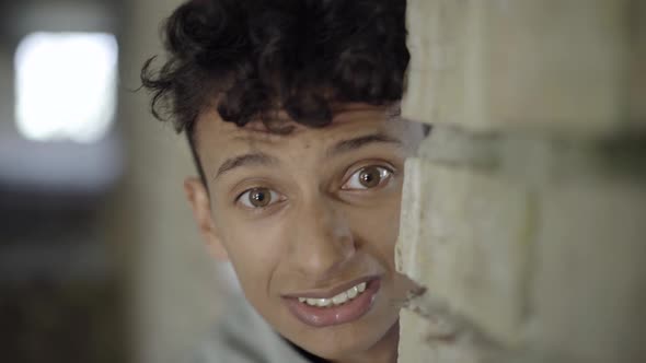 Close-up Face of Terrified Young Man Hiding Behind Brick Wall on Slums. Portrait of Scared Gypsy or