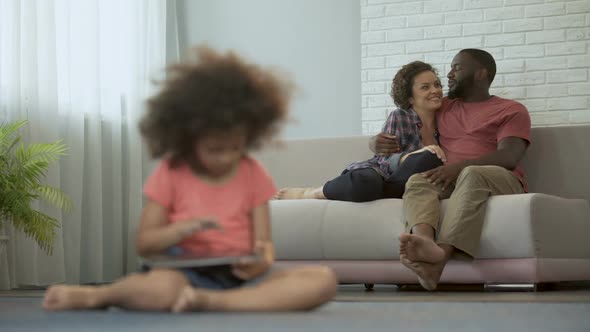 Young Parents Enjoying Joint Pastime Watching Their Daughter Playing on Tablet