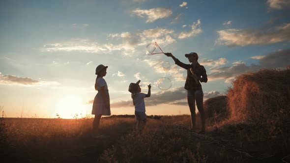 Young Mother and Two Children in the Sunset Catches Soap Bubbles in Meadow. Relax with Children in