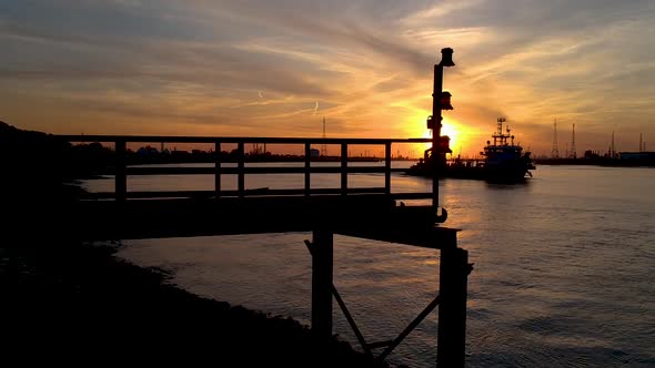 Antwerp international port. Tug boat passes at sunset. Crane down shot.