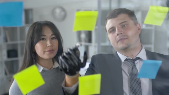 Man with Bionic Hand Discussing Plans in Sticky Notes with Female Colleague