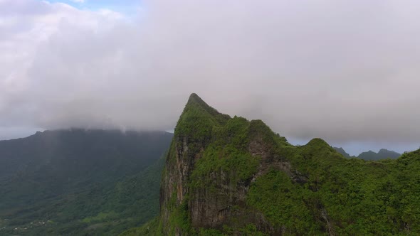 Aerial view of a mountain peak covered by vegetation and low altitude clouds in French Polynesia