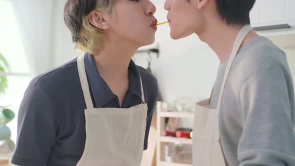 Asian handsome man gay family eating pasta by mouth to mouth together in kitchen in house.