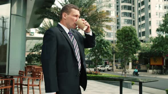 The Shot Moves Around a Businessman Standing on Street in the City Center Who and Drinks Hot