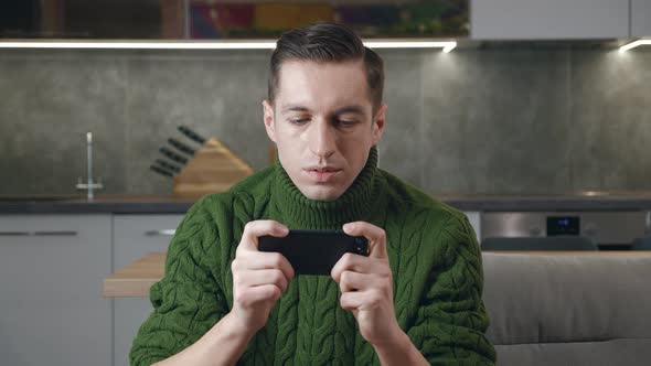 Young Man in Sweater Playing on His Smartphone Exciting Mobile Application Winning a Racing Game