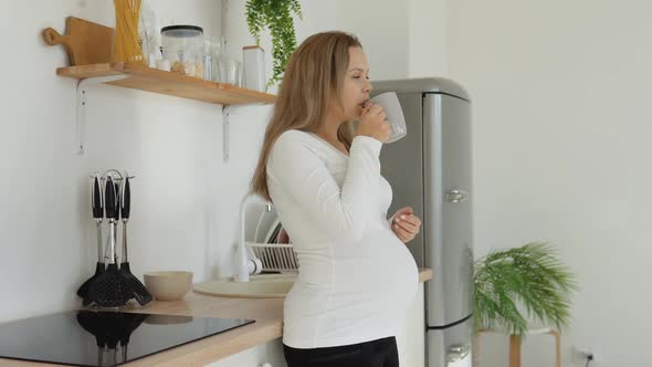 Pregnant Woman Drinking From a Cup in the Kitchen