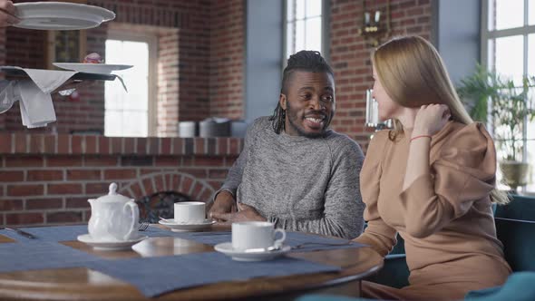 Portrait of Positive Couple Talking Sitting in Restaurant with Tea As Waiter Bringing Order in Slow