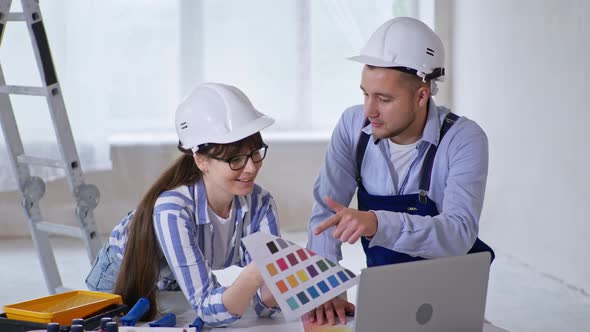 Professional Male and Female Builders in Protective Helmets and Colors in Their Hands Discuss Design