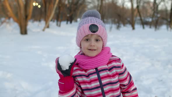 Smiling Child Kid Girl Throws Snowball Into Camera Having Fun Fooling Around in Winter Park Forest