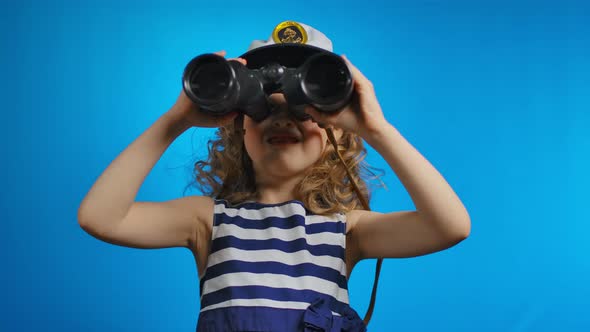 A Little Cute Curly Blond Girl is Looking at the Sky Through the Binoculars