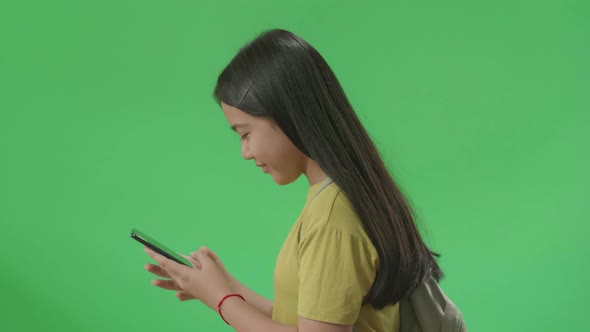Side View Of Asian Girl Student Use Mobile Phone And Walking On Green Screen Chroma Key