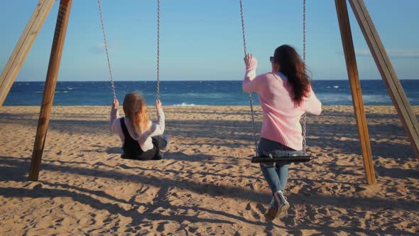 Happy Girls Friends Swing on Swings at Beach