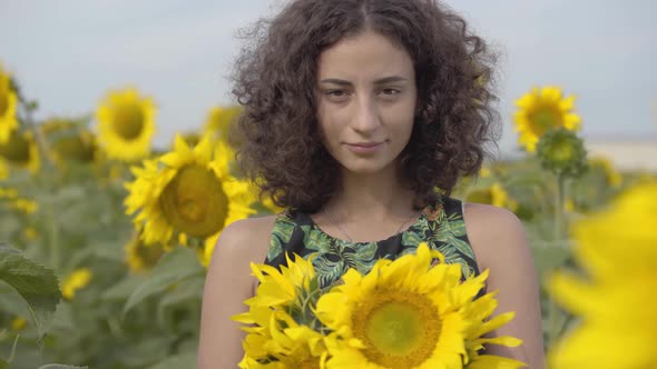 Portrait of Beautiful Curly Playful Girl Looking at the Camera Smiling Standing in the Sunflower