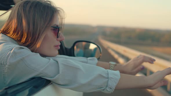 A Young Adult Woman Rides Along a Rural Road in an Open Cabriolet Enjoying the Wind and Freedom