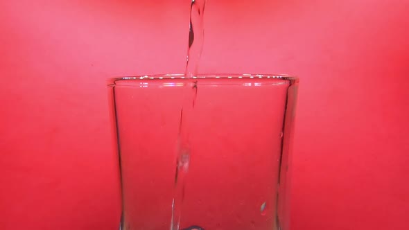 Close up shot of pouring water in glass. Pink background. Static