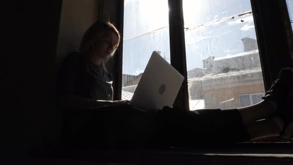 Woman sitting on the window sill with her laptop
