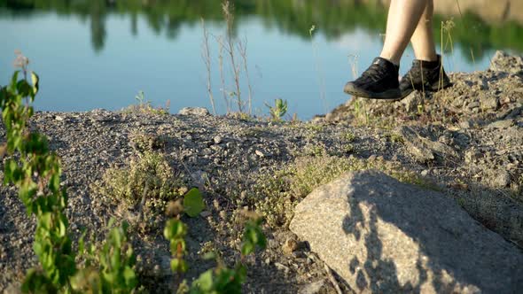 A man in black sneakers walks on stony ground along the lake on a sunny day of summer.