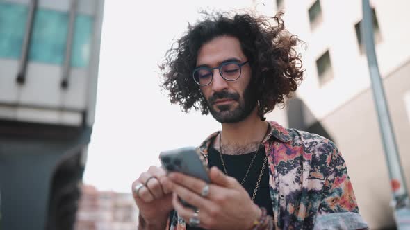 Pensive curly-haired bearded man in eyeglasses looking at phone and around