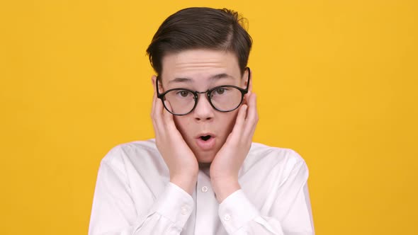 Shocked Teen Boy Looking At Camera Touching Face Yellow Background