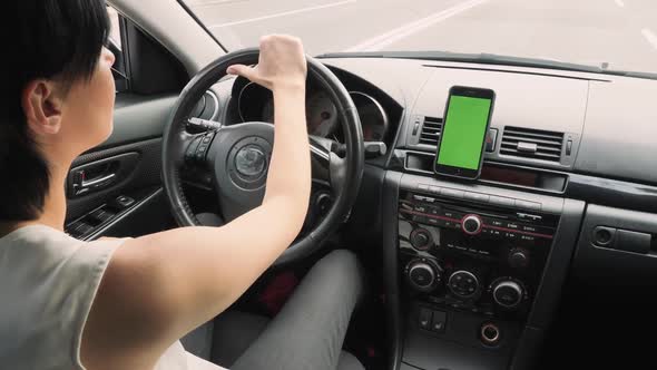 A Woman Is Driving a Car Along a High-speed Highway, on the Dashboard a Phone with a Green Screen.