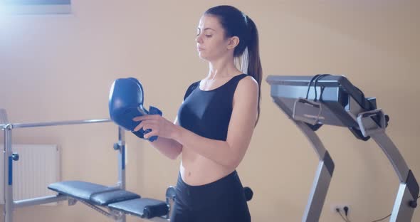 Middle Shot Portrait of Confident Slim Fit Woman Putting on Boxing Glove in Gym