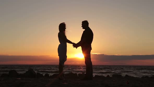 Happy Couple Holding Hands on Beach at Sunset