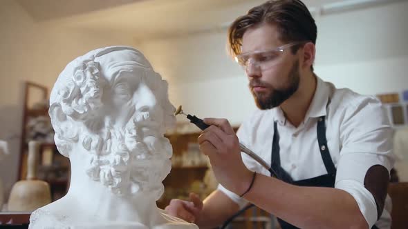 Modern Bearded Sculptor which Polishing the Sculpture's Head Details in Special Glasses