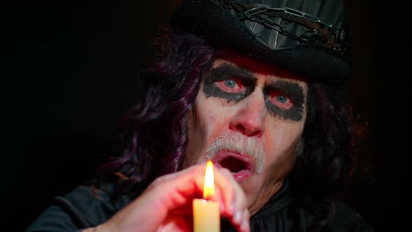 Frightening Creepy Senior Man with Halloween Witcher Makeup Looking at Candle Conjure Hex Wiz