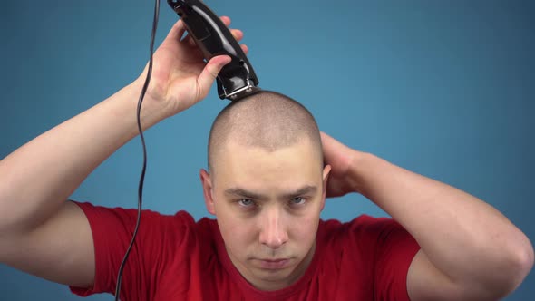 The Bald Young Man Insolently Shaves His Head. A Man Cuts His Hair Using a Hairdressing Machine on a