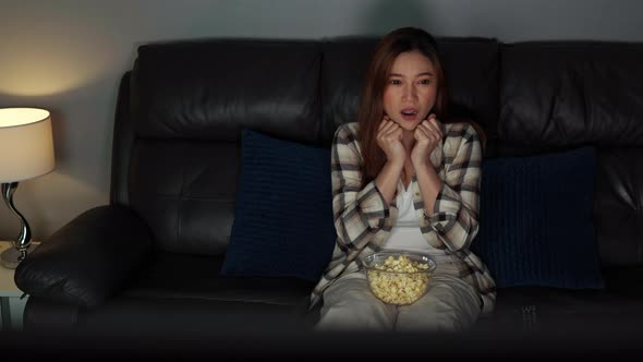 scared young woman is watching horror movie TV on sofa at night