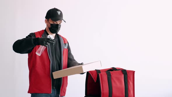 Deliveryman in a Mask and Gloves Is Spraying Antiseptic on a Pizza Box