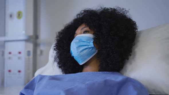 Portrait of african american female patient wearing face mask lying on hospital bed