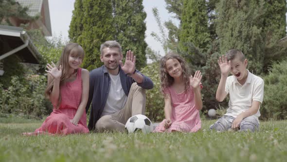 Happy Family Sitting on the Grass in the Garden Together. Mother, Father, Son, and Daughter Looking