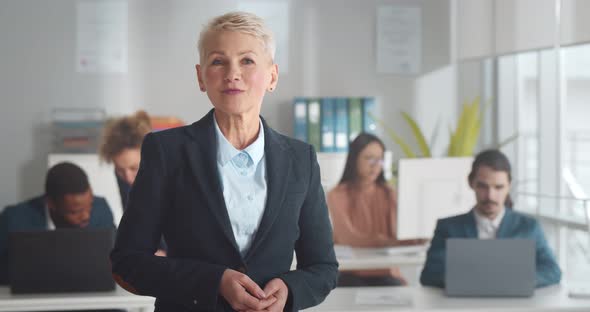 Mature Businesswoman Looking at Camera and Talking Standing in Coworking Office