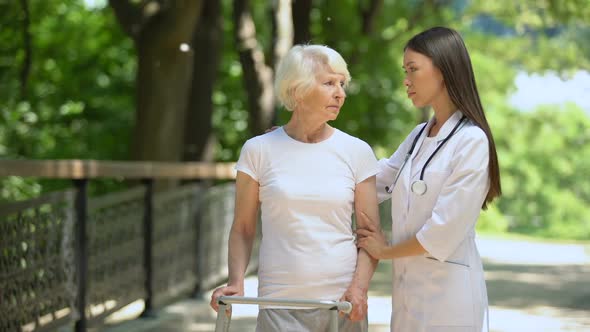 Upset Senior Woman With Walking Frame and Female Therapist Looking at Camera