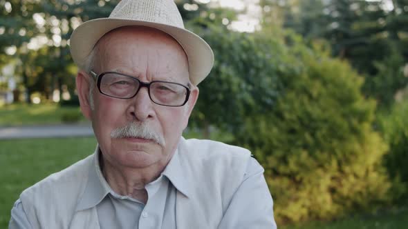 Portrait of Thoughtful Senior Man with Glasses in Hat Looking Sadly Into Camera