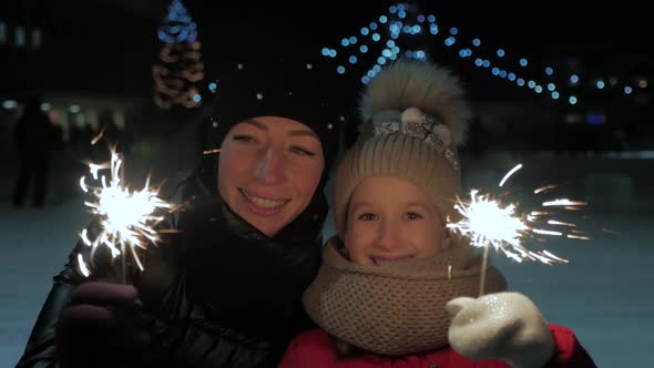 Happy Family Mother and Little Girl Playing with Bengal Lights at Outdoor. Burning Bengal Lights in