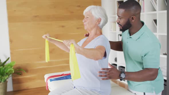 Video of happy caucasian senior woman exercising with african american male physiotherapist