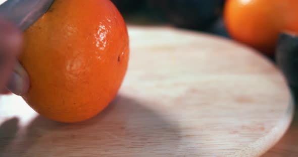 Close Still Shot of a Hand Grabbing a Clementine and Cutting it in Half With a Knife on a Wooden Sur