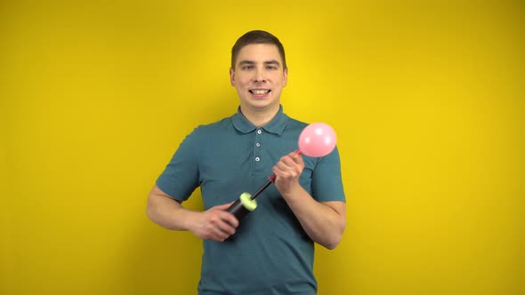 A Young Man Inflates a Pink Balloon with a Pump on a Yellow Background. Man in a Green Polo.