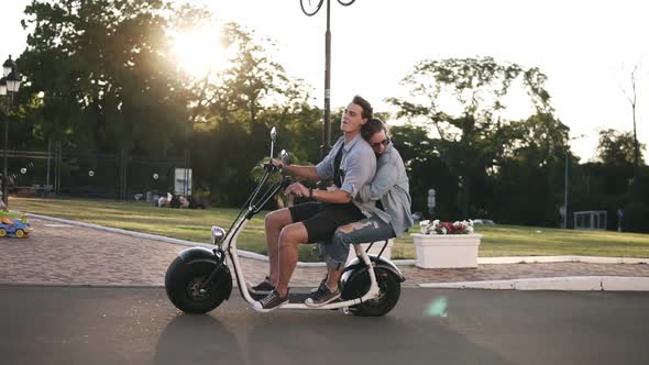 Confident Man in Blue Shirt Driving Scooter While His Girlfriend Embracing Him