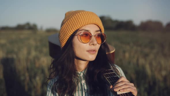 Beautiful Asian Hipster Woman Gutar Player Walking on a Sunny Field with a Acoustic