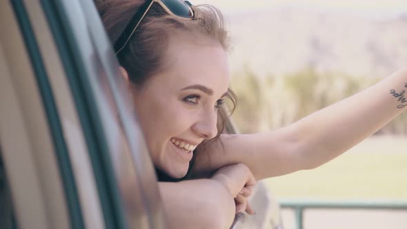 Smiling Lady Looks Out of Car Window Waves Hands on Warm Day
