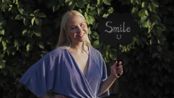 A Beautiful Young Girl Is Smiling and Holding a Sign That Says "Smile". Call for Good Mood. Smile