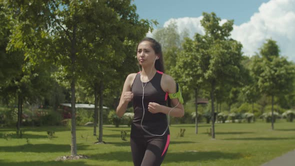 Fit Woman in Headphones Running on Park Lane