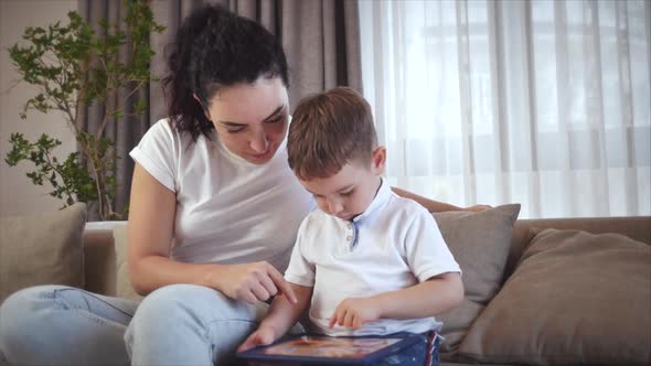 Cute Family Happy Mom and Cute Little Kid Son Look at Screen of a Tablet Cell Phone, Mother with