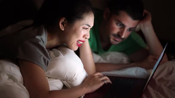 Happy multiethnic couple watching movie on laptop in bed