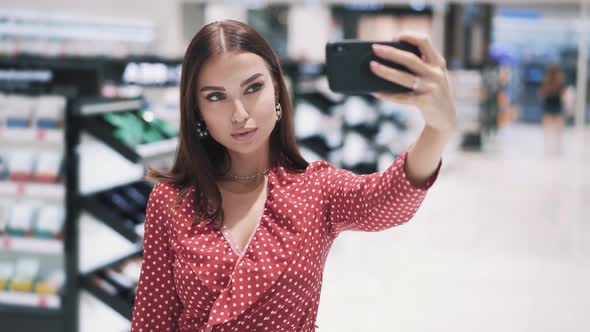 Young Pretty Caucasian Brunette Girl in Red Dress Makes Selfie on Smartphone