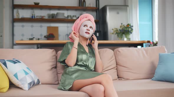 Female in Facial Mask, Robe and Towel Having Phone Call Resting on Sofa