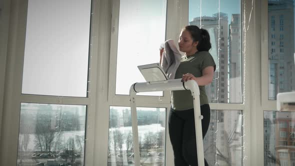 Attractive sportive woman is wiping face with towel during intense fitness exercises on treadmill